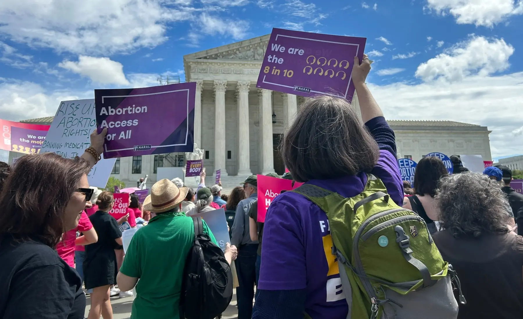 Members hold up reproductive freedom signs with their backs to the camera, facing the U.S. Supreme Court within a crowd.