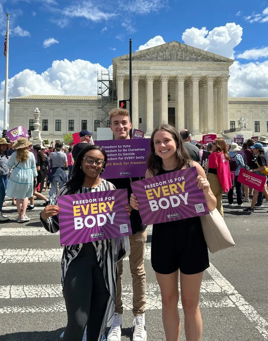 Reproductive freedom supporters stand outside of the Supreme Court for a rally, holding "Freedom is for Everybody" signs.